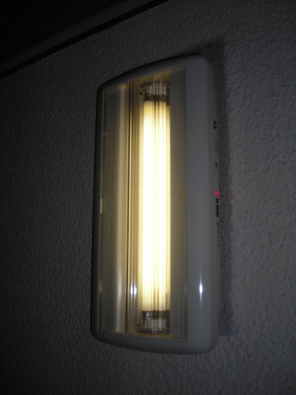 Wall-mounted emergency luminaire lit on a dark wall with a red status indicator
