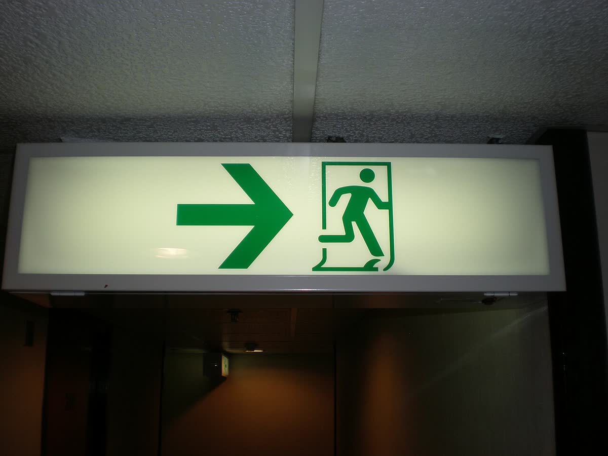 Green exit sign hanging above a corridor, corridor darker in the distance