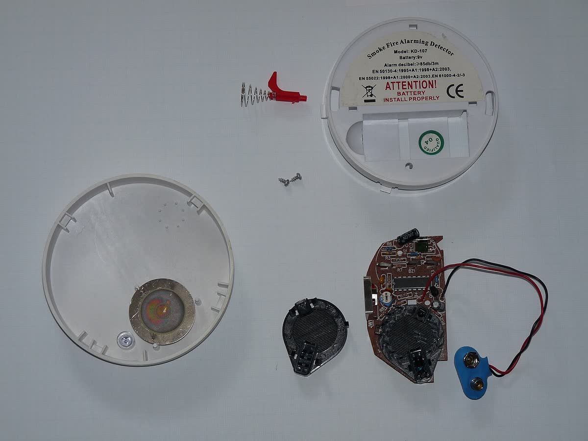 A disassembled optical smoke detector: base, optical chamber and circuit board